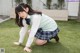 A young woman in a school uniform crouching on the grass.