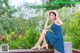 A woman in a blue dress and straw hat sitting on a bench.