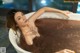 A woman sitting in a bathtub filled with brown liquid.