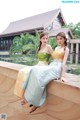 Two young women sitting on a wall next to a pond.