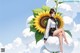 A woman sitting on top of a cloud next to a sunflower.