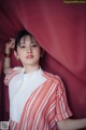 A woman in a red and white striped shirt leaning against a red curtain.