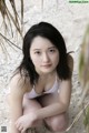 A woman in a white bikini sitting on the sand.